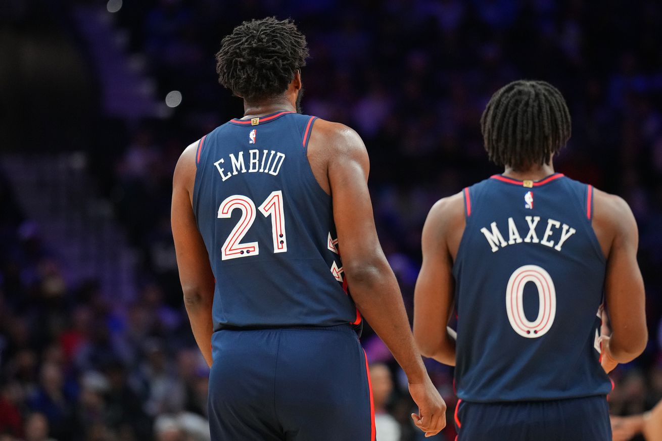 View from behind of Joel Embiid standing next to Tyrese Maxey.