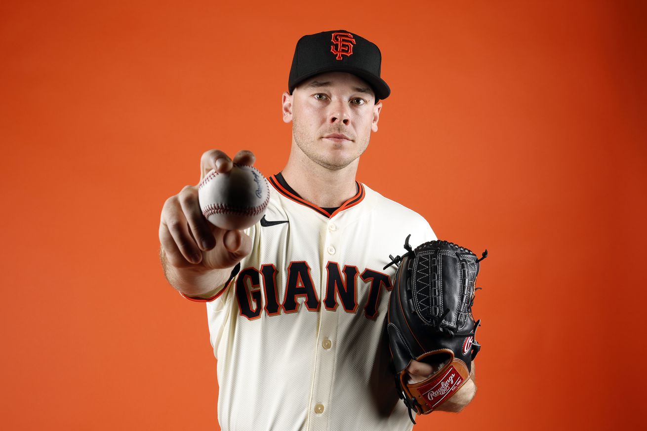 Daulton Jefferies posing in front of an orange background, holding out a baseball. 