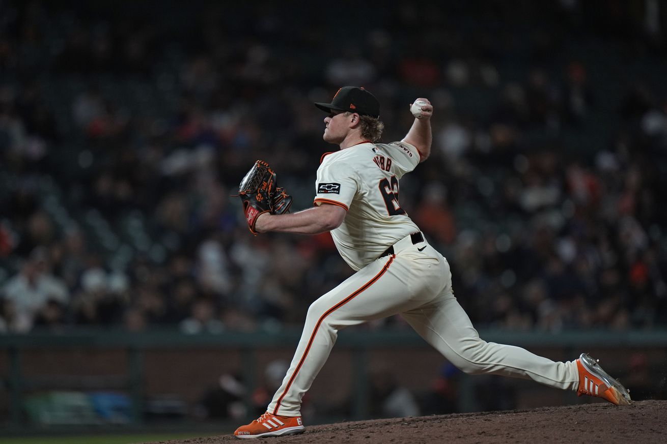 View from the first base side of Logan Webb in the middle of throwing a pitch.