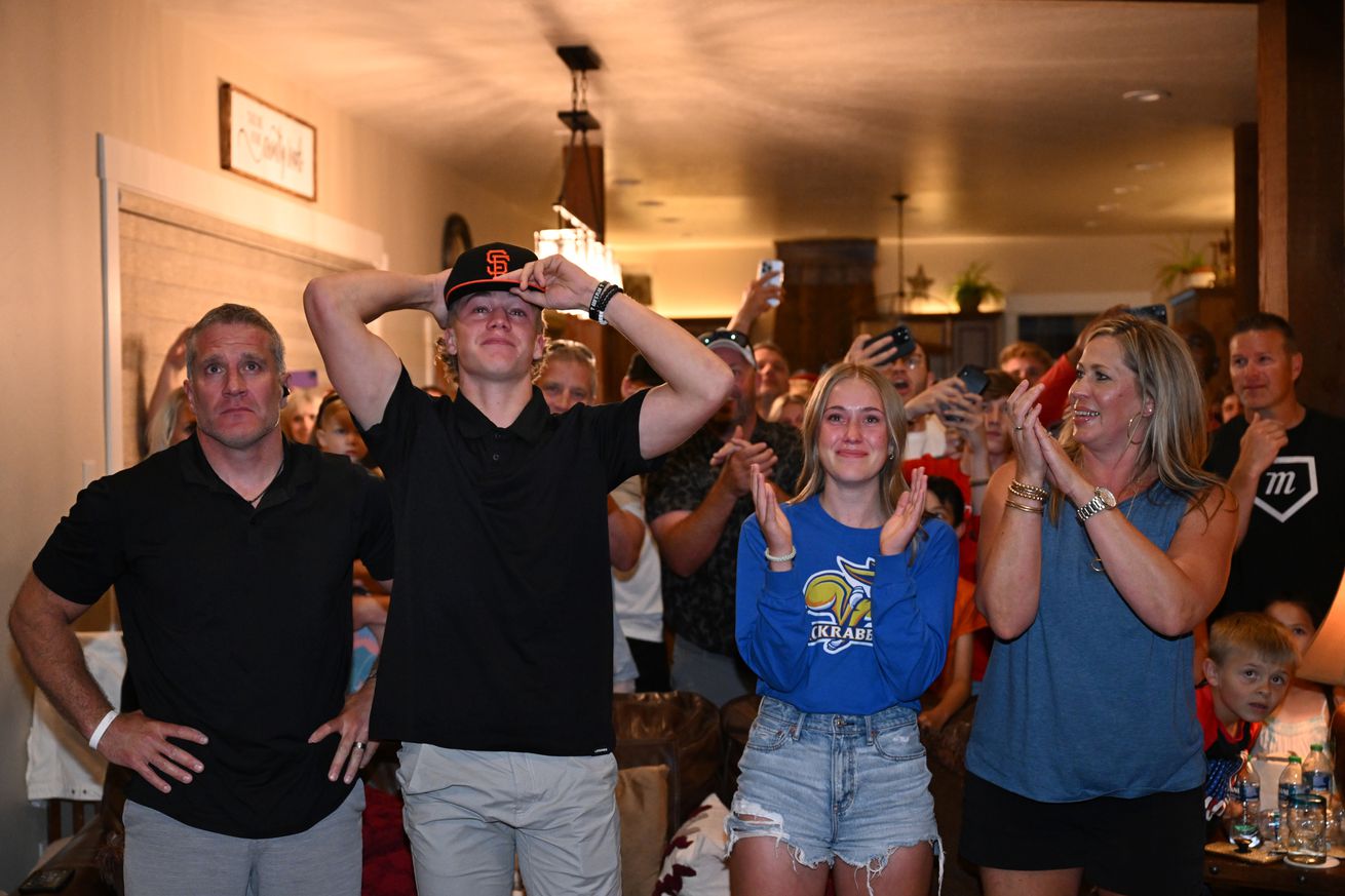 Walker Martin putting on a Giants hat after getting drafted, while his family celebrates around him.