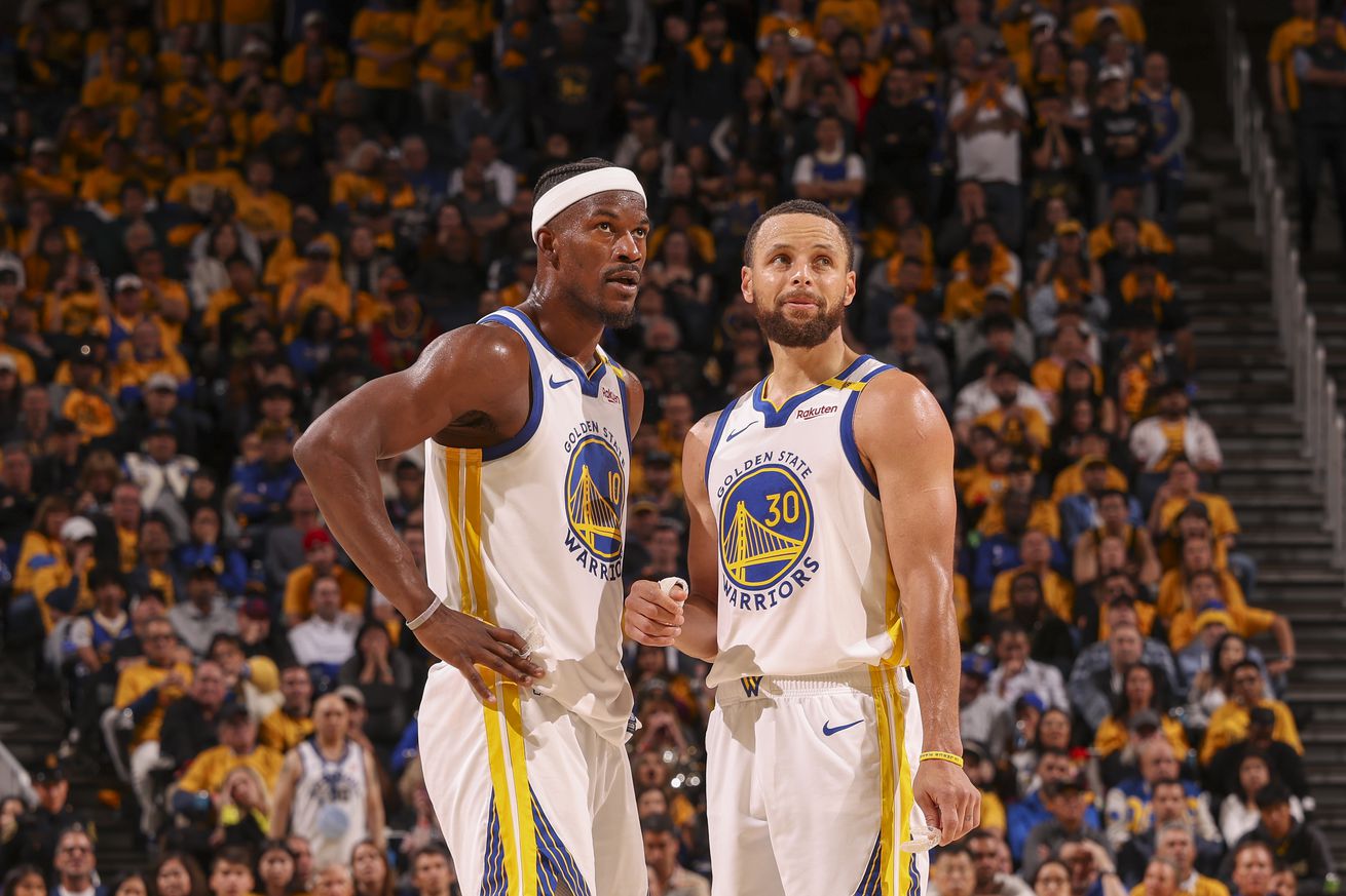 Jimmy Butler III and Steph Curry standing next to each other at midcourt, looking up at the scoreboard.