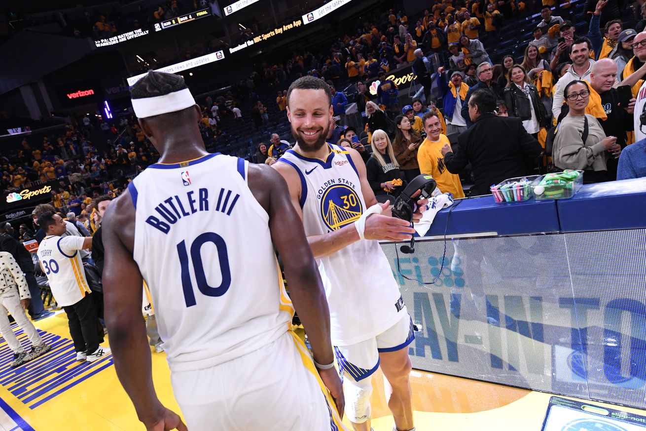 Steph Curry, facing the camera, smiling and preparing to dap Jimmy Butler III, facing away from the camera.