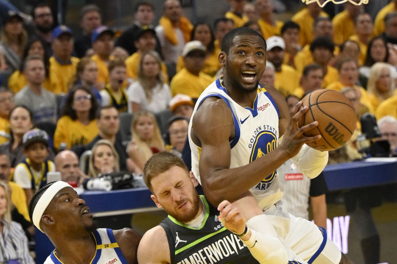 Jonathan Kuminga awkwardly in the air trying to shoot a layup while on top of a crouched Donte DiVincenzo, while Jimmy Butler III looks on.