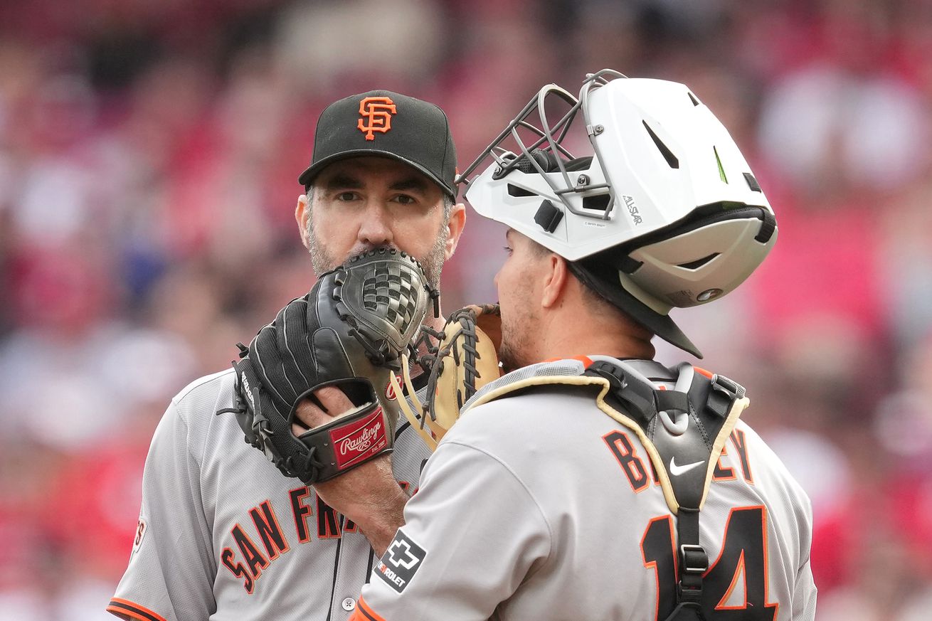 Justin Verlander and Patrick Bailey talking on the mound, covering their face with their gloves.