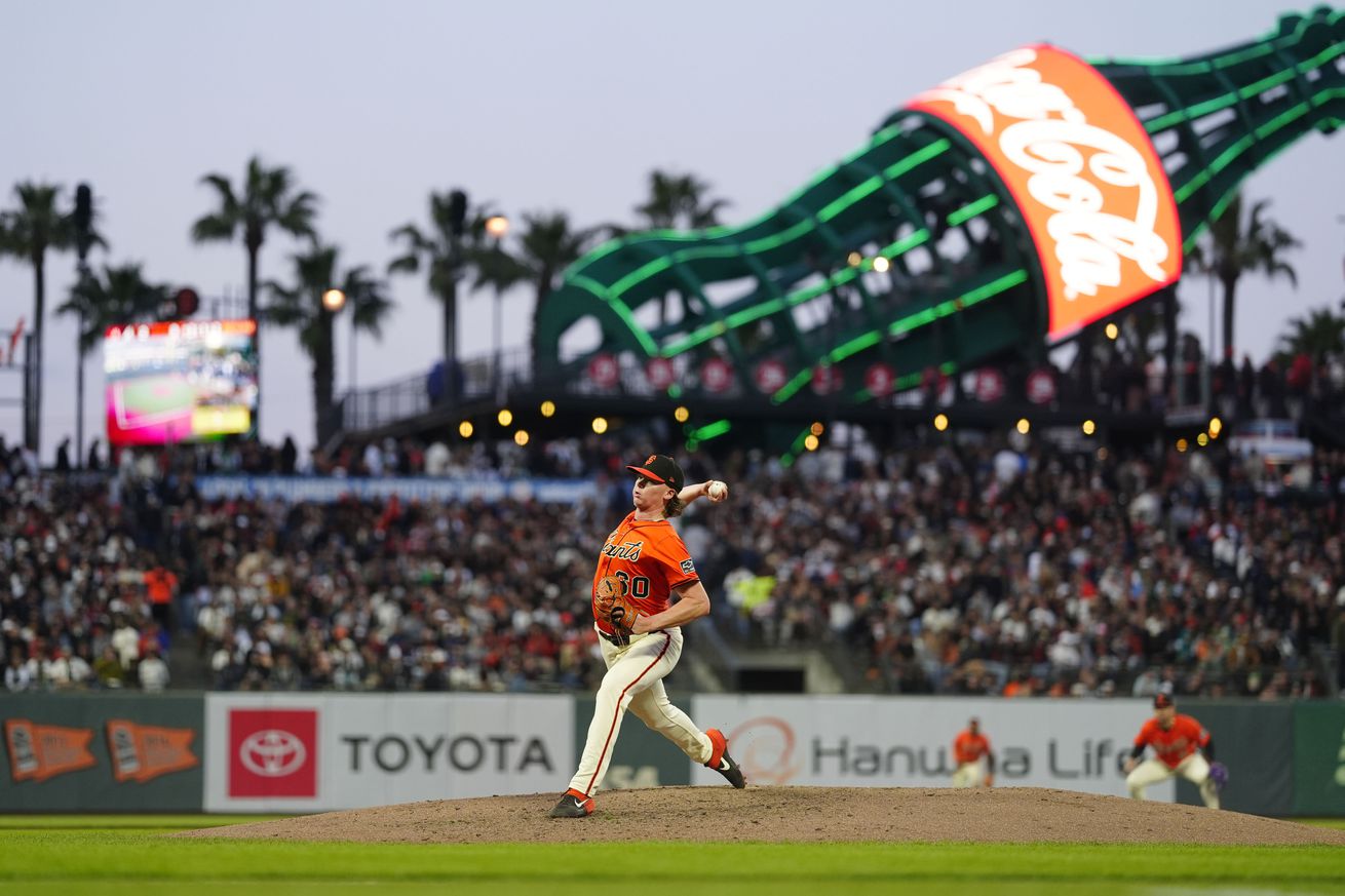 Hayden Birdsong throwing a pitch at night in an orange Giants jersey with the coke bottle behind him. 