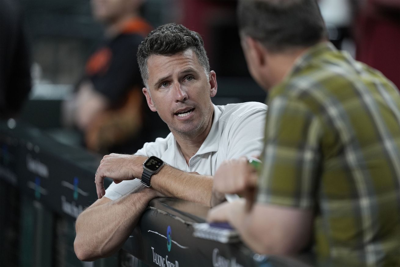 Buster Posey leaning over a dugout railing, talking to someone. 